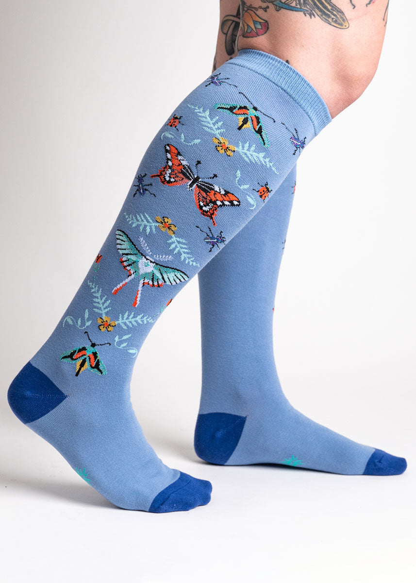Blue knee socks for women with a design of bugs such as a monarch butterfly, moths, beetles, ladybugs, and floral designs, with hints of rainbow glitter.