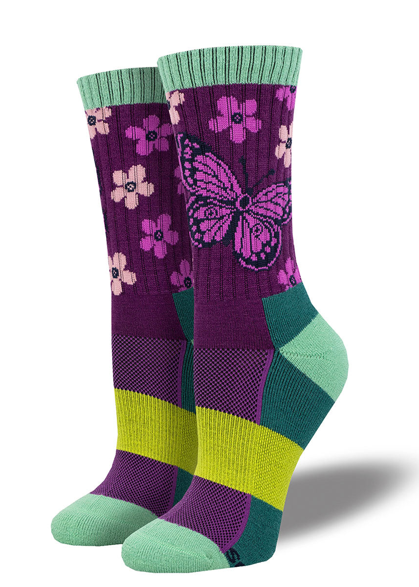 Purple hiking socks for women with sections of teal and lime green that depict a pink butterfly design against a repeating pattern of pink and light pink flowers.