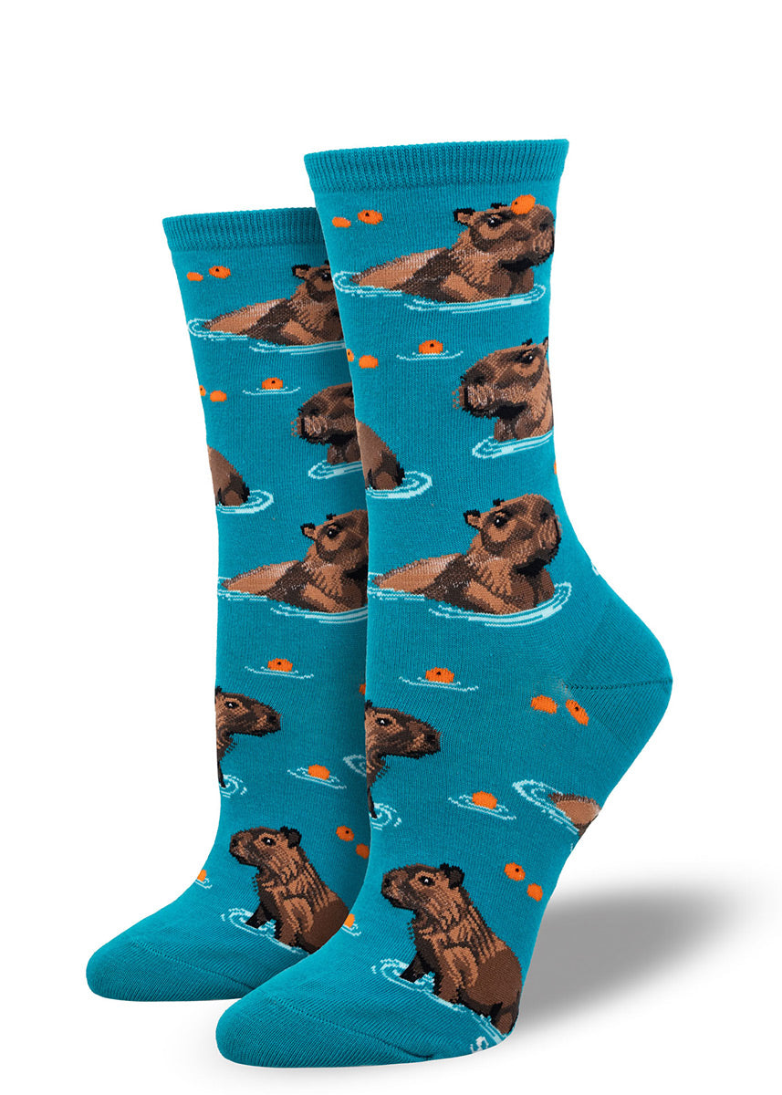 Blue crew socks for women that show several capybara hanging out in the water with some fruit around them.