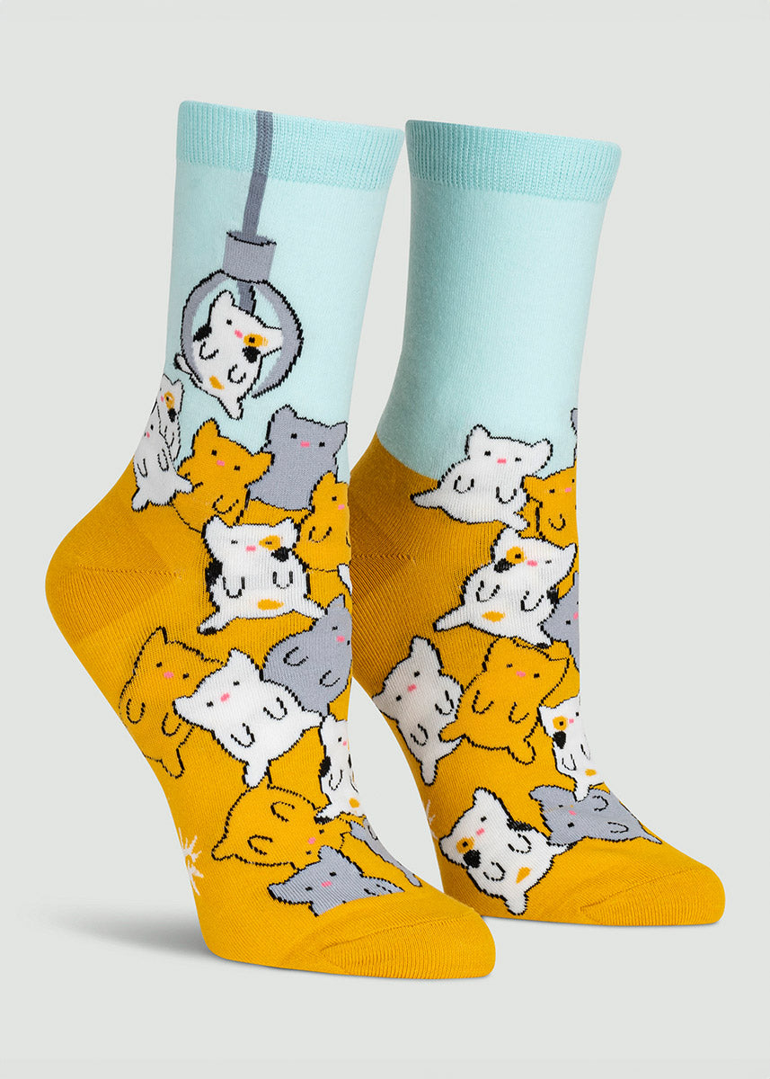 Gold and aqua women&#39;s crew socks feature a claw game design with different color cats waiting to be lifted out by a giant mechanical claw.
