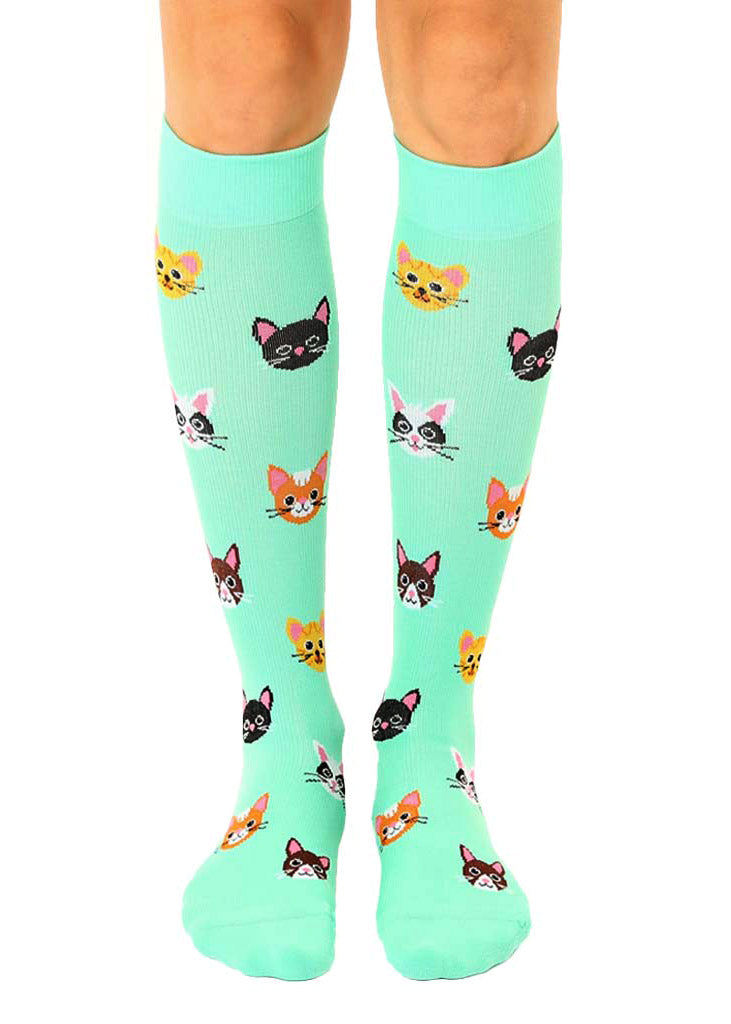 Aqua knee-high compression socks with an allover pattern of various cat faces, including black, orange tabby, tuxedo cats and more.