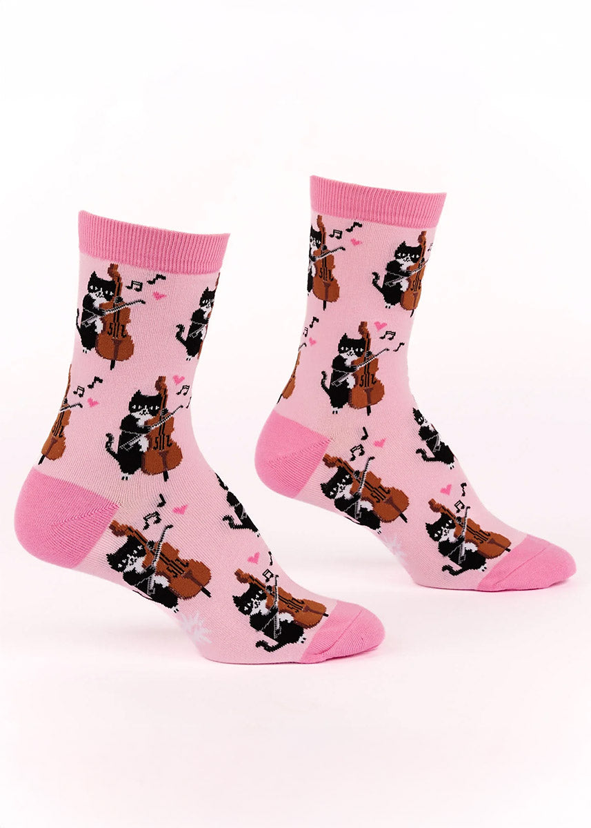 Pink crew socks for women with an allover pattern of black and white cats playing the cello surrounded by music notes and hearts.