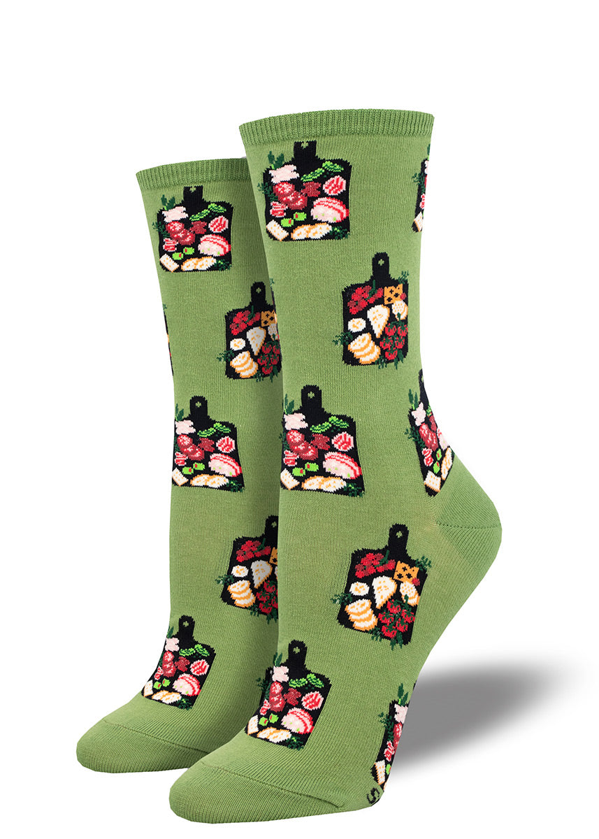 Women&#39;s crew socks with an allover pattern of charcuterie boards arranged with meats, cheeses and fruits, all on a solid green background.