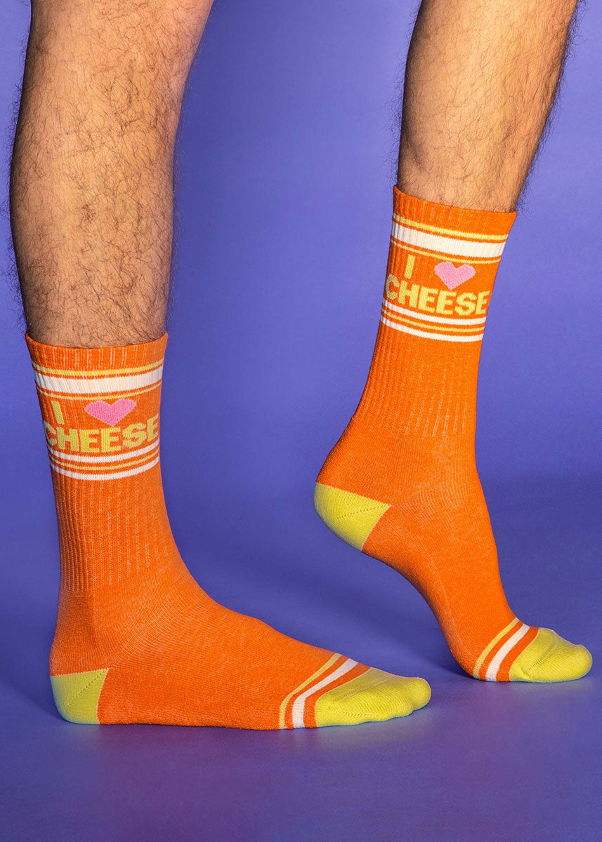 A model wearing socks that read &quot;I Heart Cheese&quot; poses against a plain purple background.