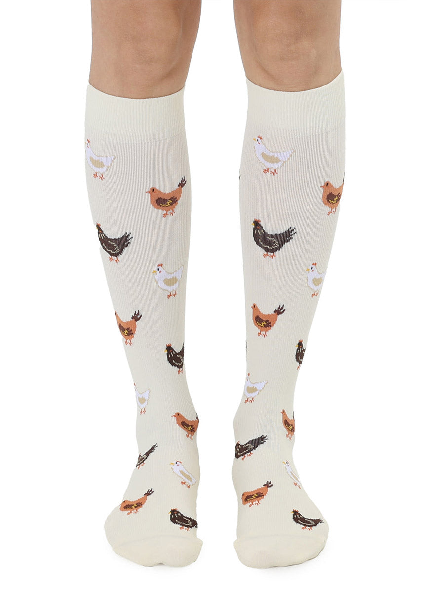 Off-white knee-high compression socks with a repeating chicken pattern worn by a person in front of a white background.