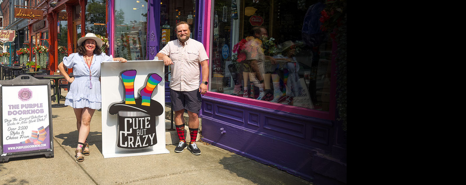 Rachel Northrup McGee and Scotty McGee hold the 'Cute But Crazy' sock store sign while standing in front of The Purple Doorknob sock shop in Ellicottville, New York.