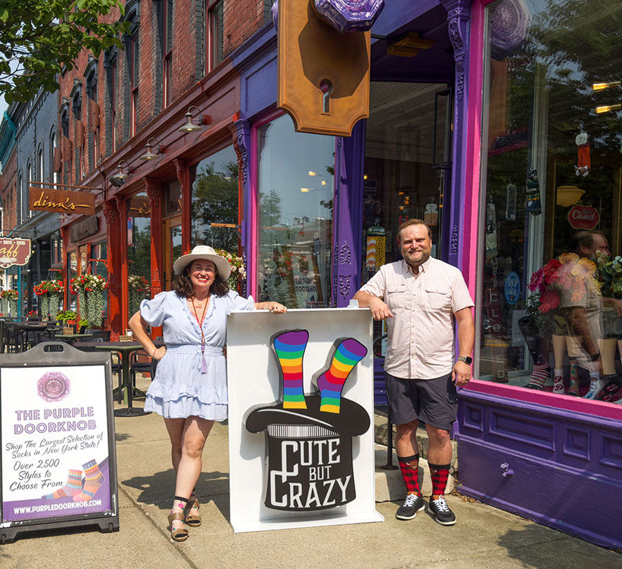 Rachel Northrup McGee and Scotty McGee hold the 'Cute But Crazy' sock store sign while standing in front of The Purple Doorknob sock shop in Ellicottville, New York.