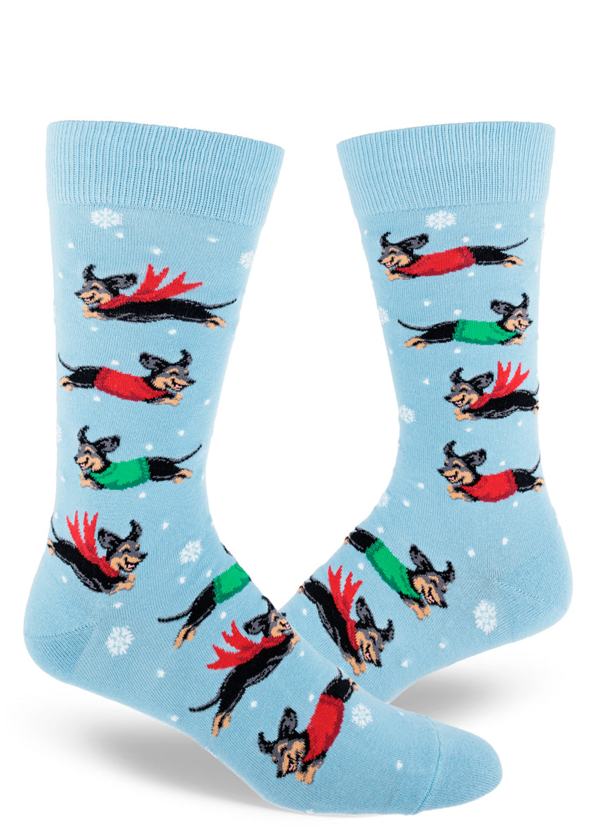 Light blue crew socks for men show a repeating pattern of snowflakes and dachshunds wearing red and green sweaters and scarves playing in the snow.