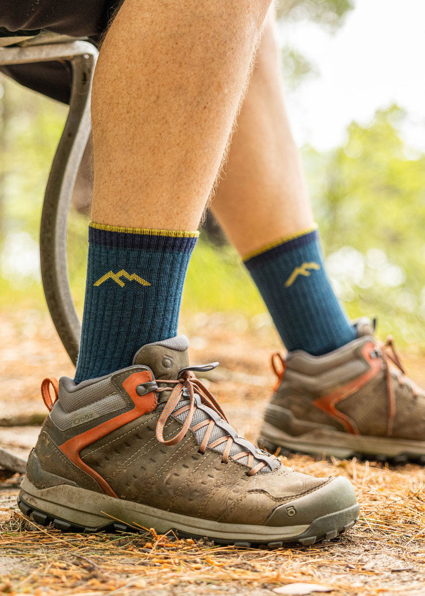 Dark teal hiking socks for men in crew length with a thin light yellow stripe at the cuff.