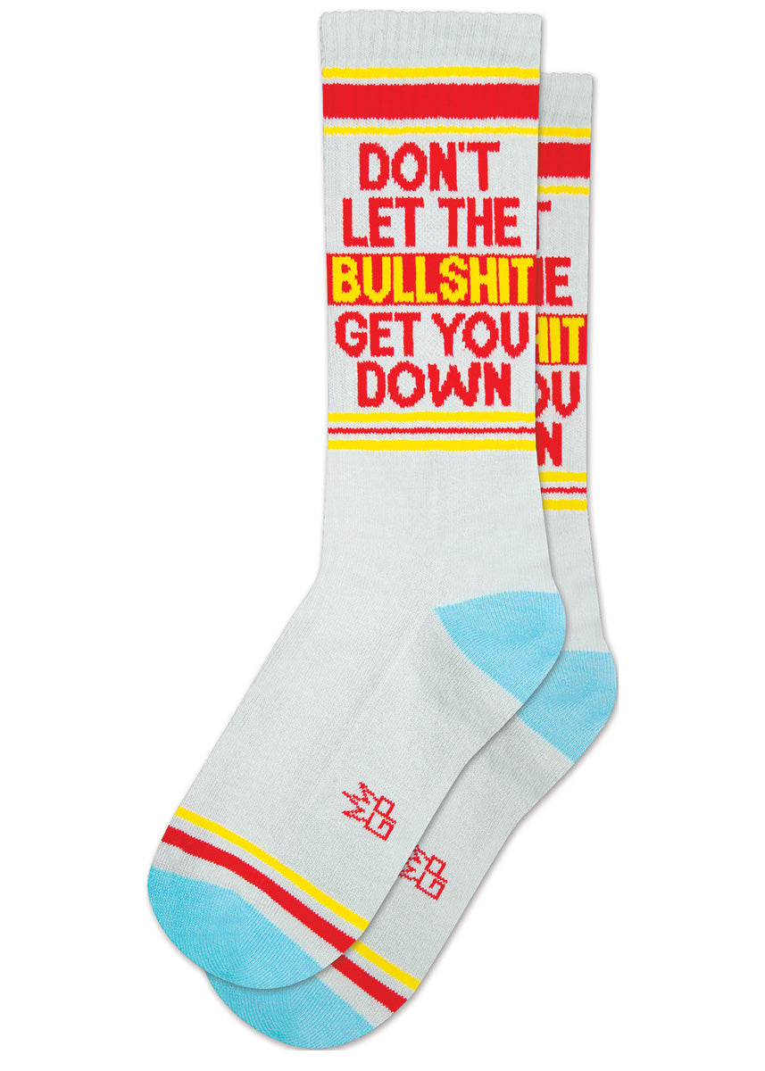 Light gray retro gym socks with light blue accents have red and yellow stripes and the phrase “ DON'T LET THE BULLSHIT GET YOU DOWN" on the leg.