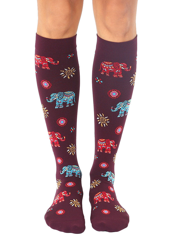 Maroon knee-high compression socks with an allover pattern of red and blue painted elephants plus abstract sun designs.