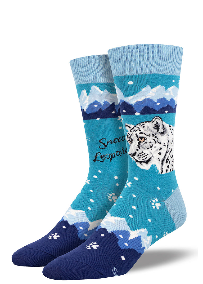 Novelty men's crew socks in shades of blue feature a snow leopard design with swirling snow, a mountain range and white paw prints.