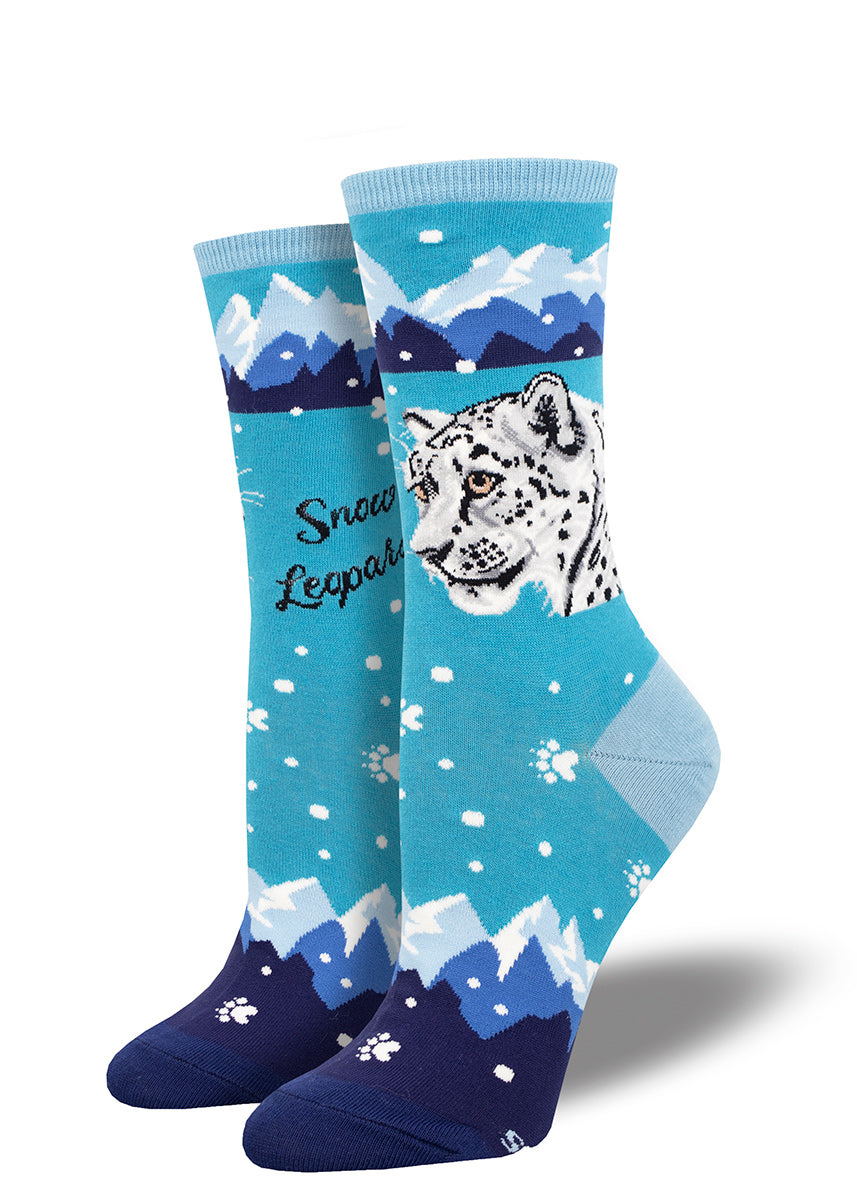 Novelty women's crew socks in shades of blue feature a snow leopard design with swirling snow, a mountain range and white paw prints.