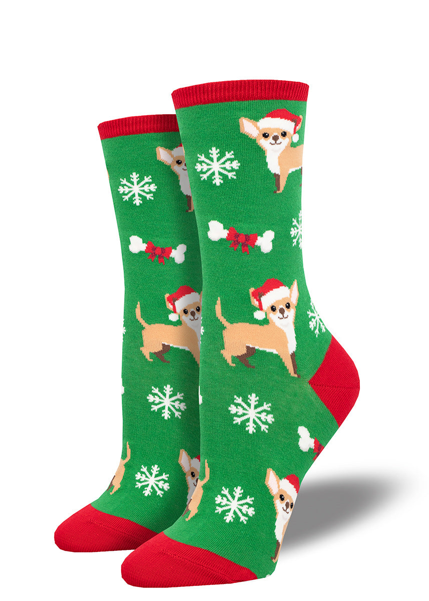 Green holiday socks for women with a red cuff, heel, and toe that feature an allover pattern of chihuahuas wearing Santa hats, dog bones tied with red ribbon, and snowflakes. 