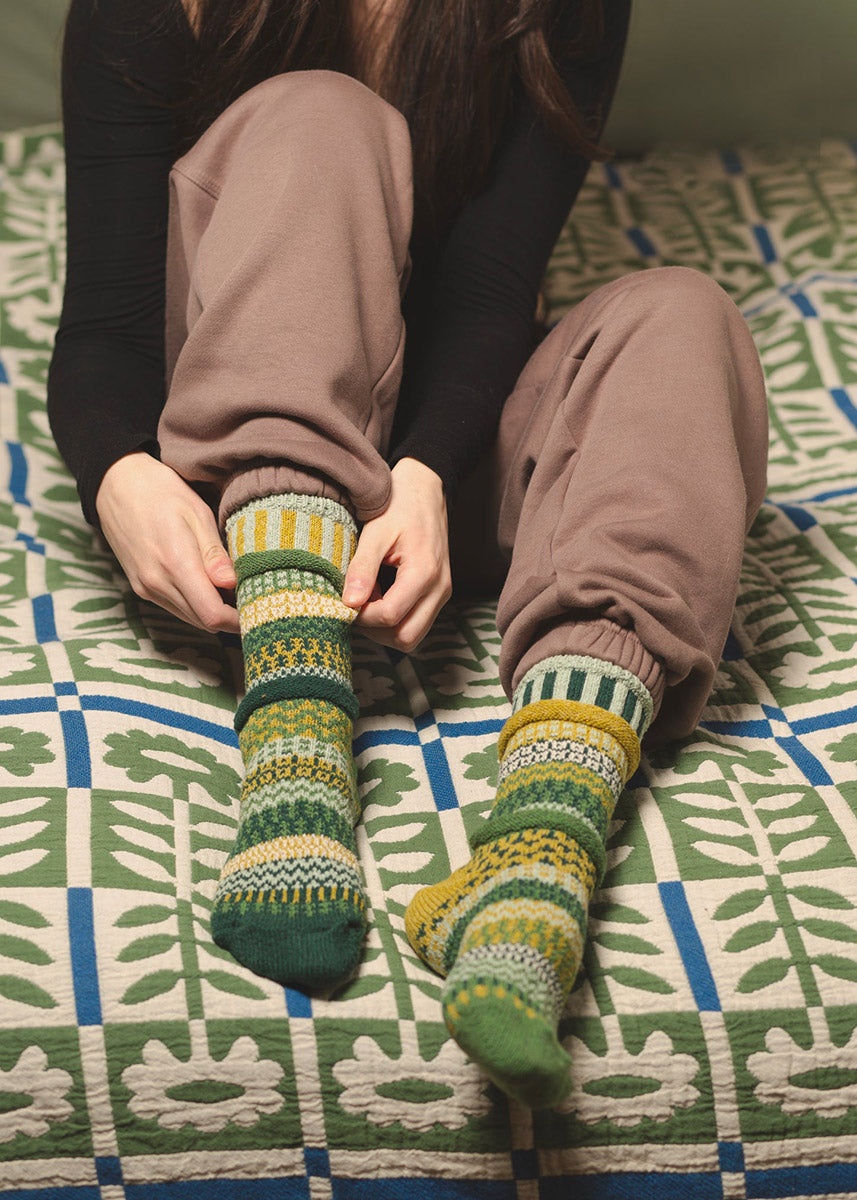 A model poses on a colorful duvet wearing Intentionally mismatched green crew socks with different sections featuring various geometric patterns.