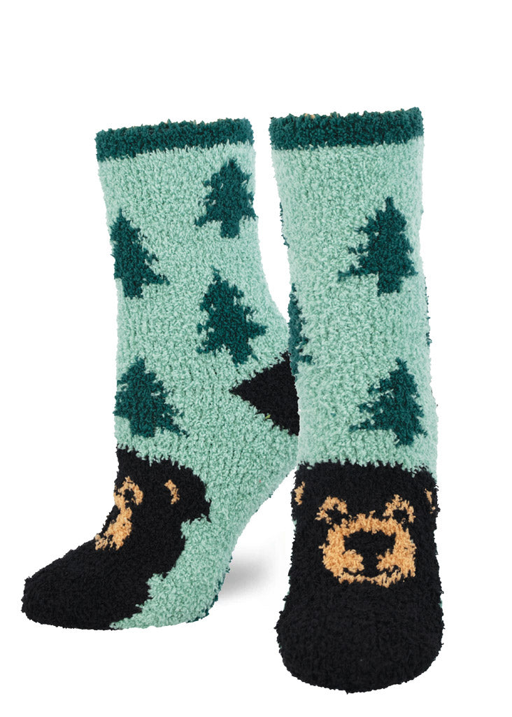 Teal fuzzy socks for women that have a repeating pattern of green pine trees and a smiling black bear face on the toe.
