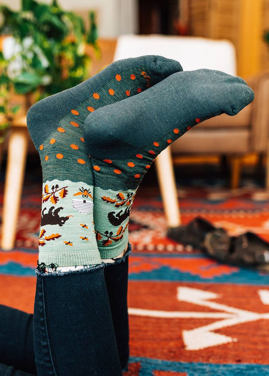 Wool crew socks with bears, beehives, orange and brown autumn foliage, plus orange polka dots on a two-toned, mossy green background.