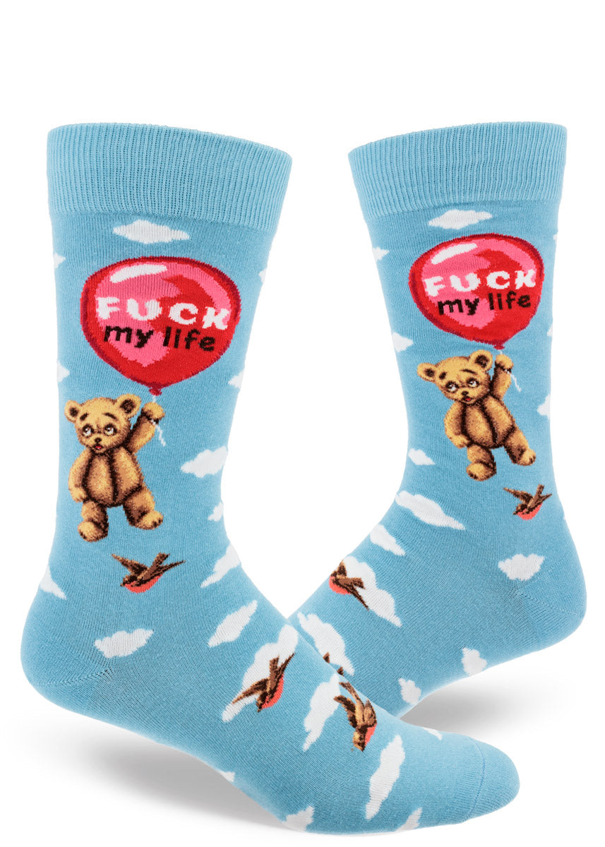 Light blue crew socks for men that feature a teddy bear holding onto a floating red balloon with the words "Fuck My Life" inside the balloon against a cloudy sky backdrop.