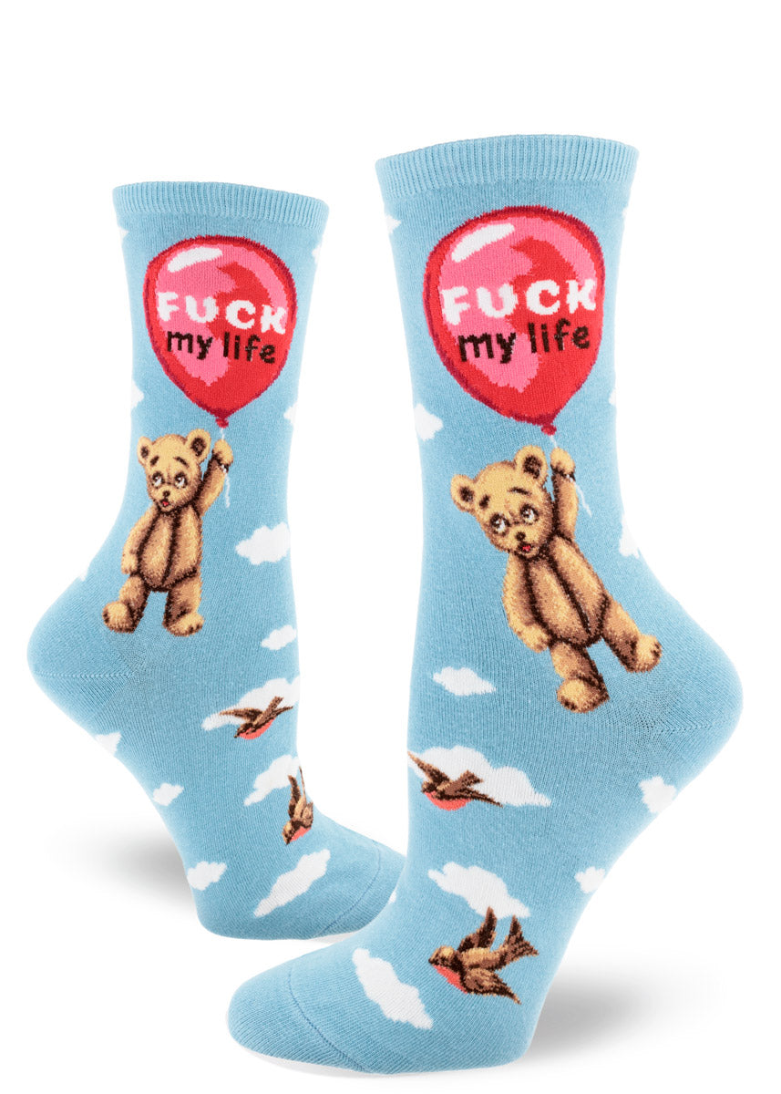 Light blue crew socks for women that feature a teddy bear holding onto a floating red balloon with the words "Fuck My Life" inside the balloon against a cloudy sky backdrop.