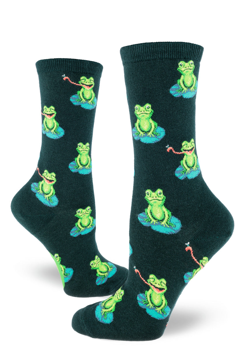 Dark green novelty socks for women show an allover pattern of green frogs sitting on lily pads with some sticking their tongue out to catch a fly.