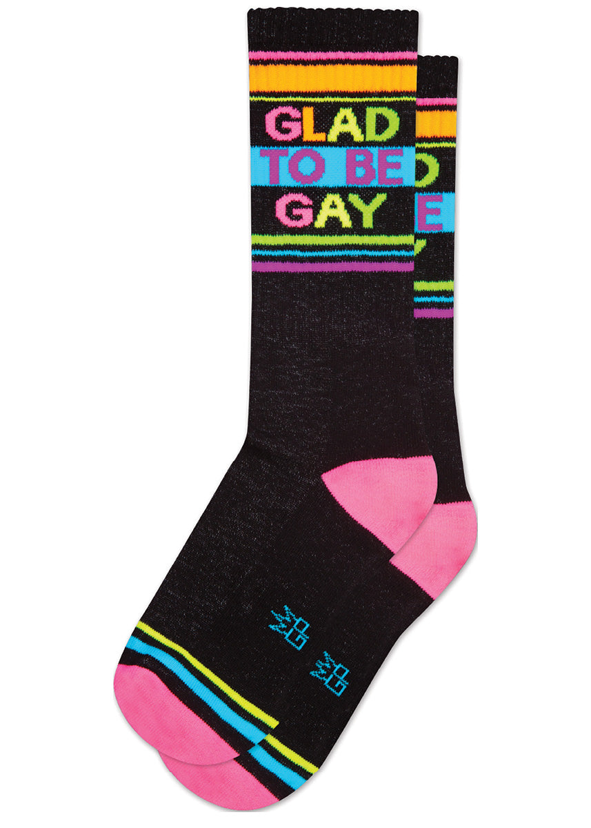 Black retro-style striped gym socks say “GLAD TO BE GAY” in neon rainbow lettering, accented with colorful neon stripes and pink neon at the heel and toe.