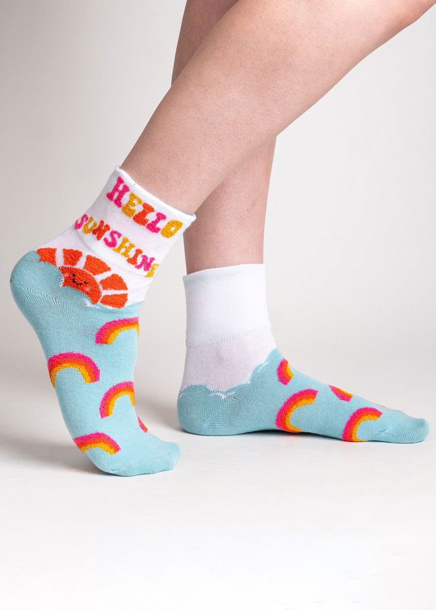 Light blue turn-cuff ankle socks for women with fuzzy pink, orange, and yellow rainbows as well as a big fuzzy orange sun and the words &quot;Hello Sunshine&quot; in fuzzy lettering when the cuff is pulled up.