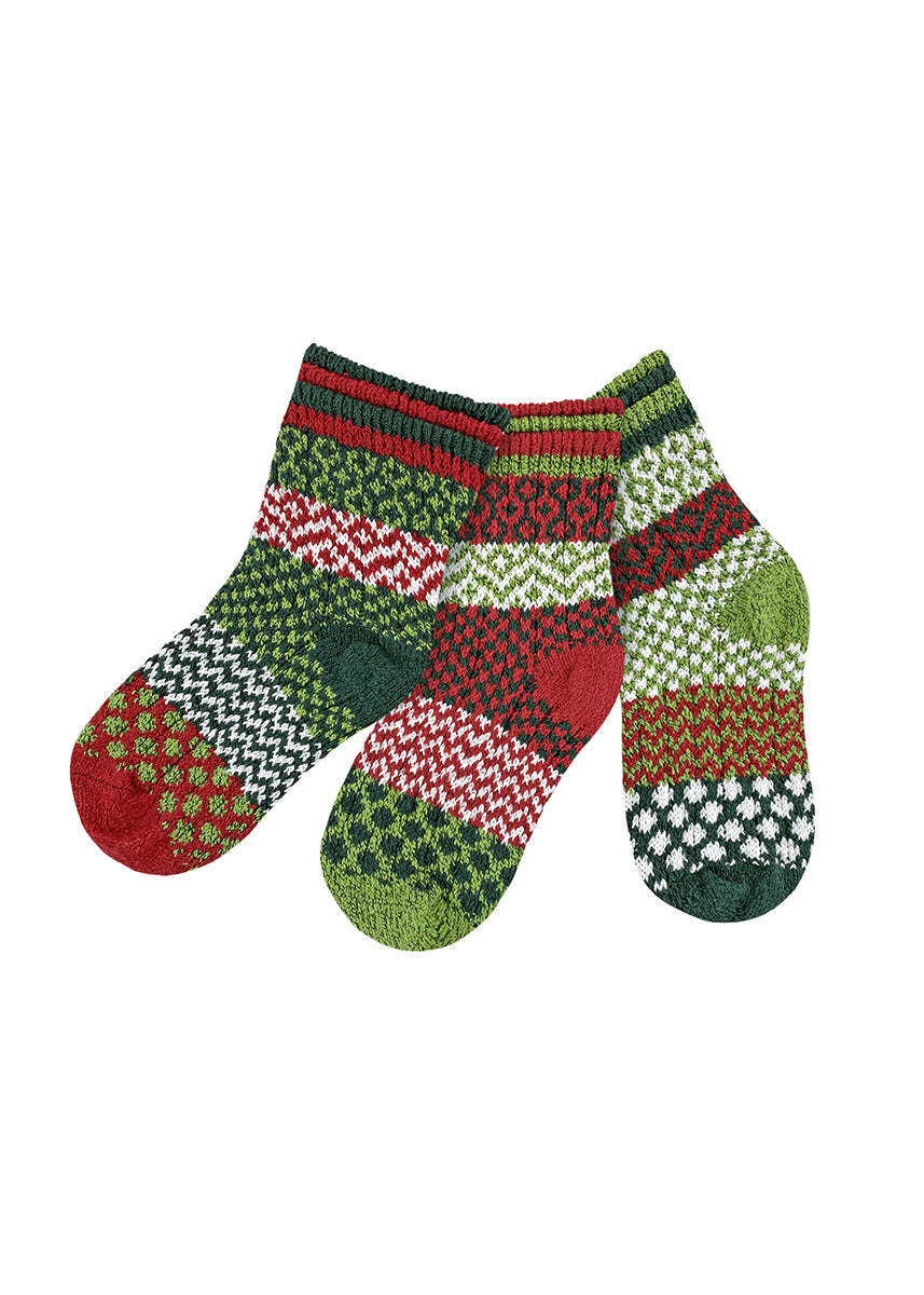 A flat lay of five different intentionally mismatched holiday crew socks for kids with different sections featuring various geometric patterns like stripes and dots in shades of red, green, and white. 