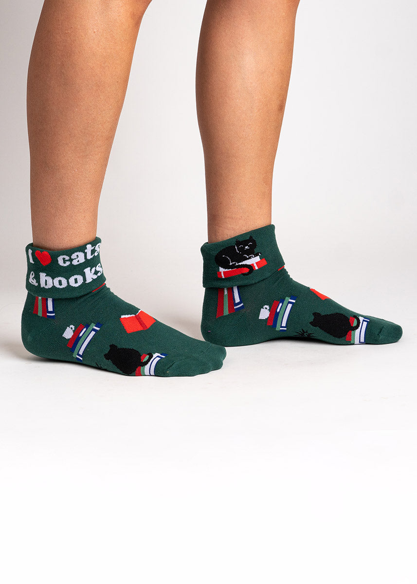 Dark green turn-cuff ankle socks for women that feature a design of black cats and colorful books and says "I love cats & books" with a red heart on the cuff. 