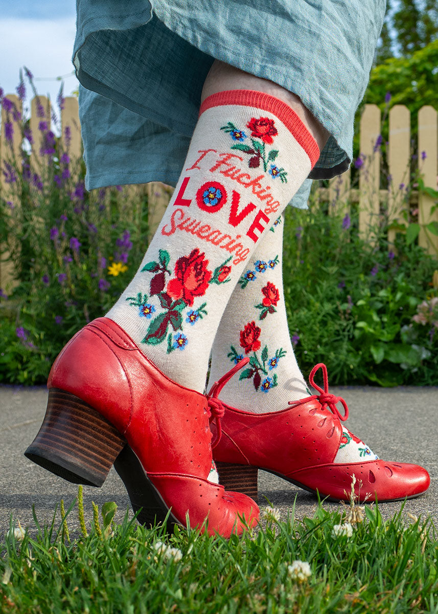 A model wearing floral novelty socks that read &quot;I Fucking Love Swearing&quot; and red heels poses outside on the sidewalk.