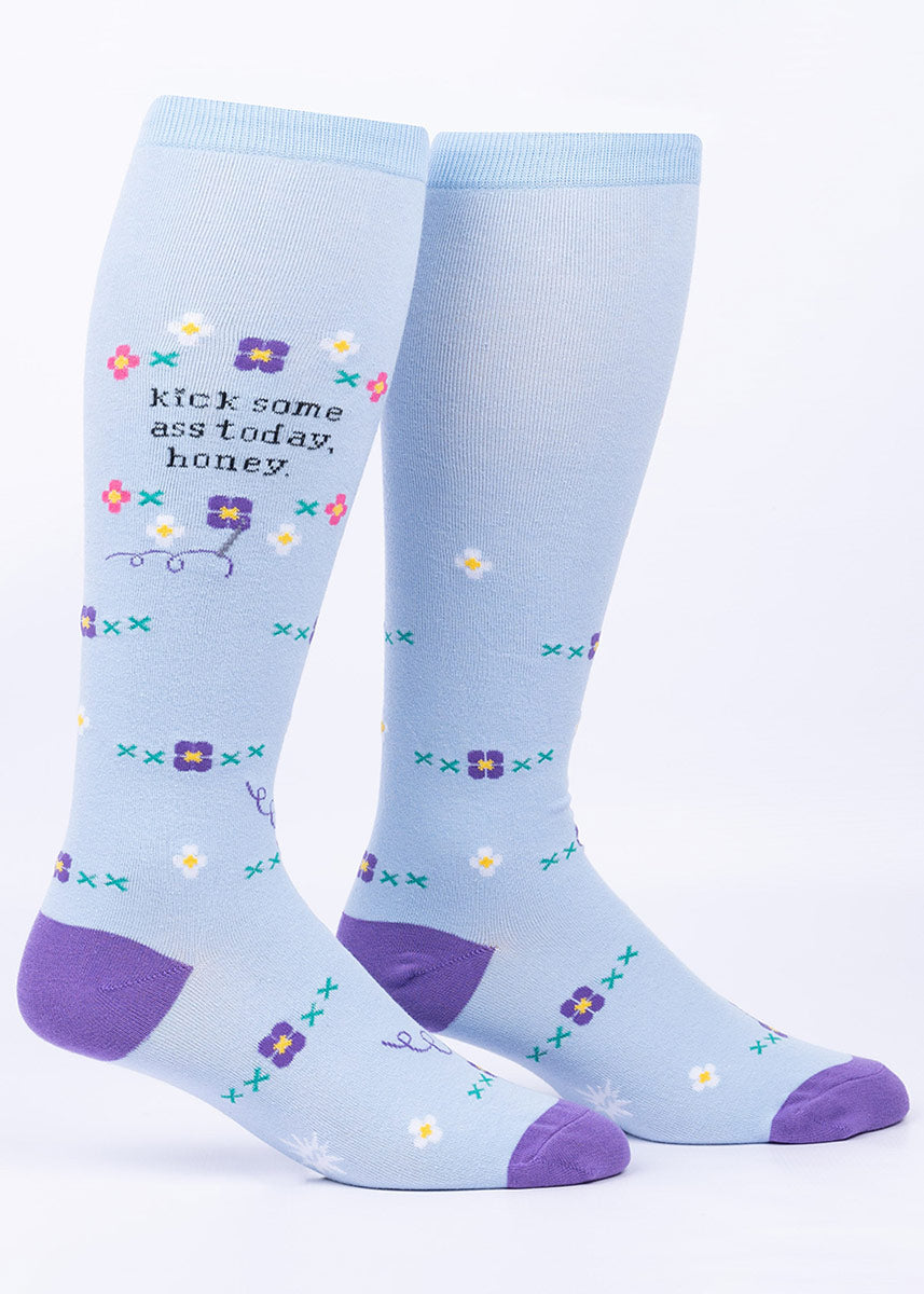 Faux embroidery knee socks in light periwinkle feature flowers in purple, pink and white as well as the words “kick some ass today, honey.” 