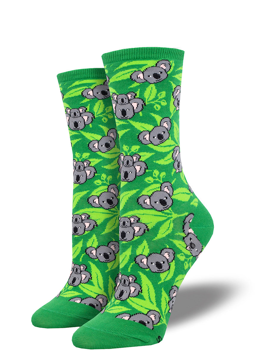 Crew socks for women with a dark and light green leafy background and an allover pattern of gray koala faces.