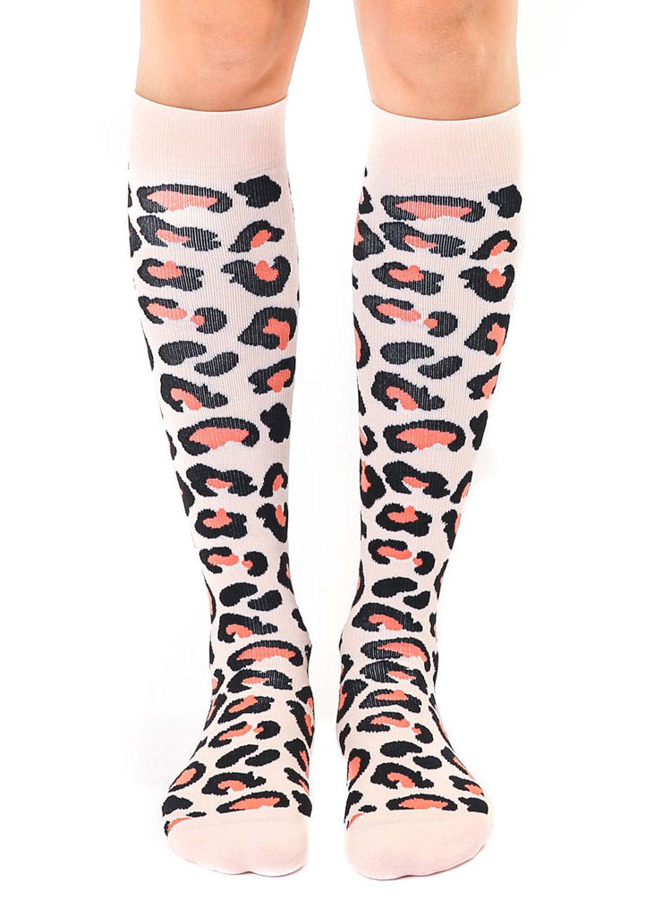 A female model poses straight-on wearing pink knee-high compression socks with an allover orange and black leopard print pattern.