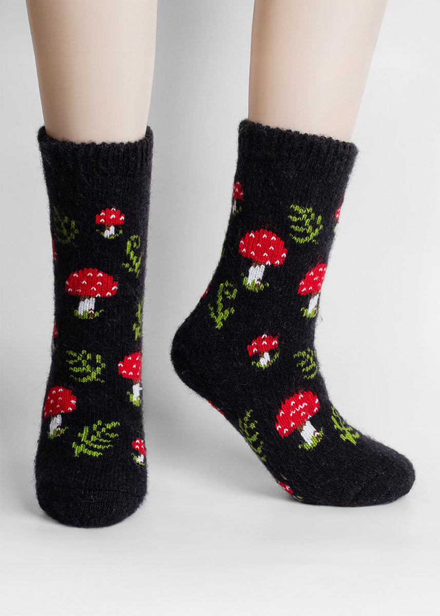 Fuzzy black wool socks with red mushroom pattern worn by a model.