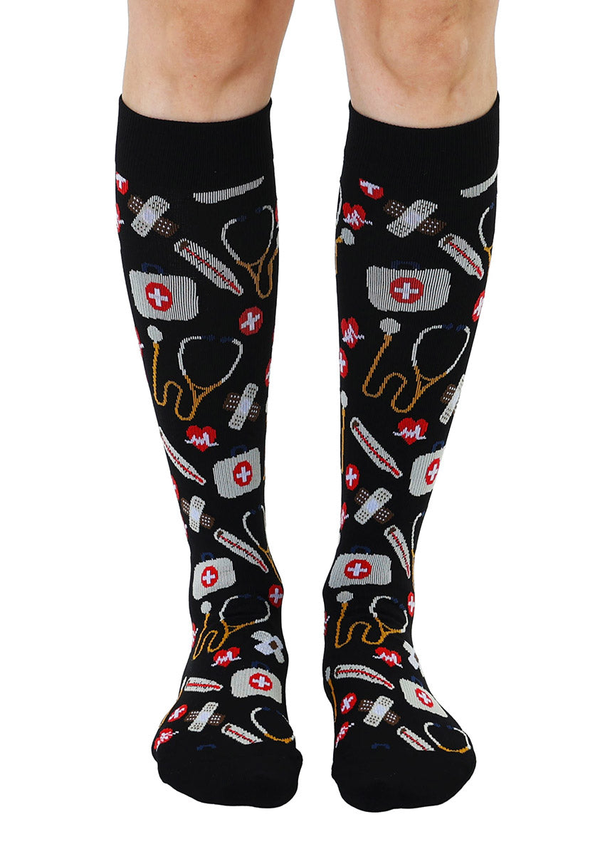 Black knee-high compression socks with medical supplies pattern worn by a model.