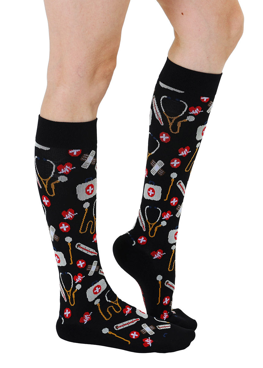 Black knee-high compression socks with medical supplies pattern worn by a model.