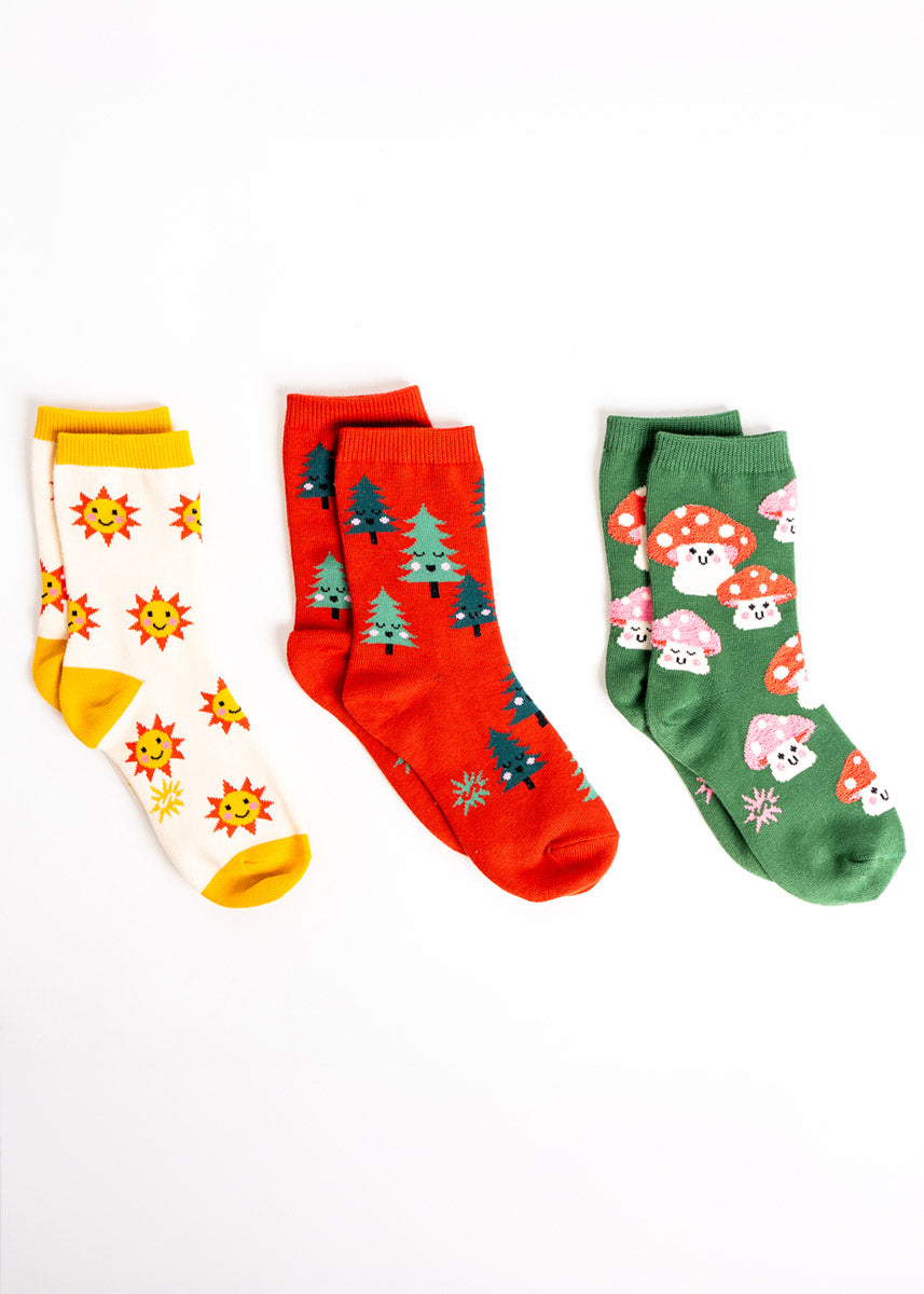 Three pairs of coordinating socks for kids: one pair features cheerful yellow suns, another has pine trees, and the third has fuzzy toadstool mushrooms.