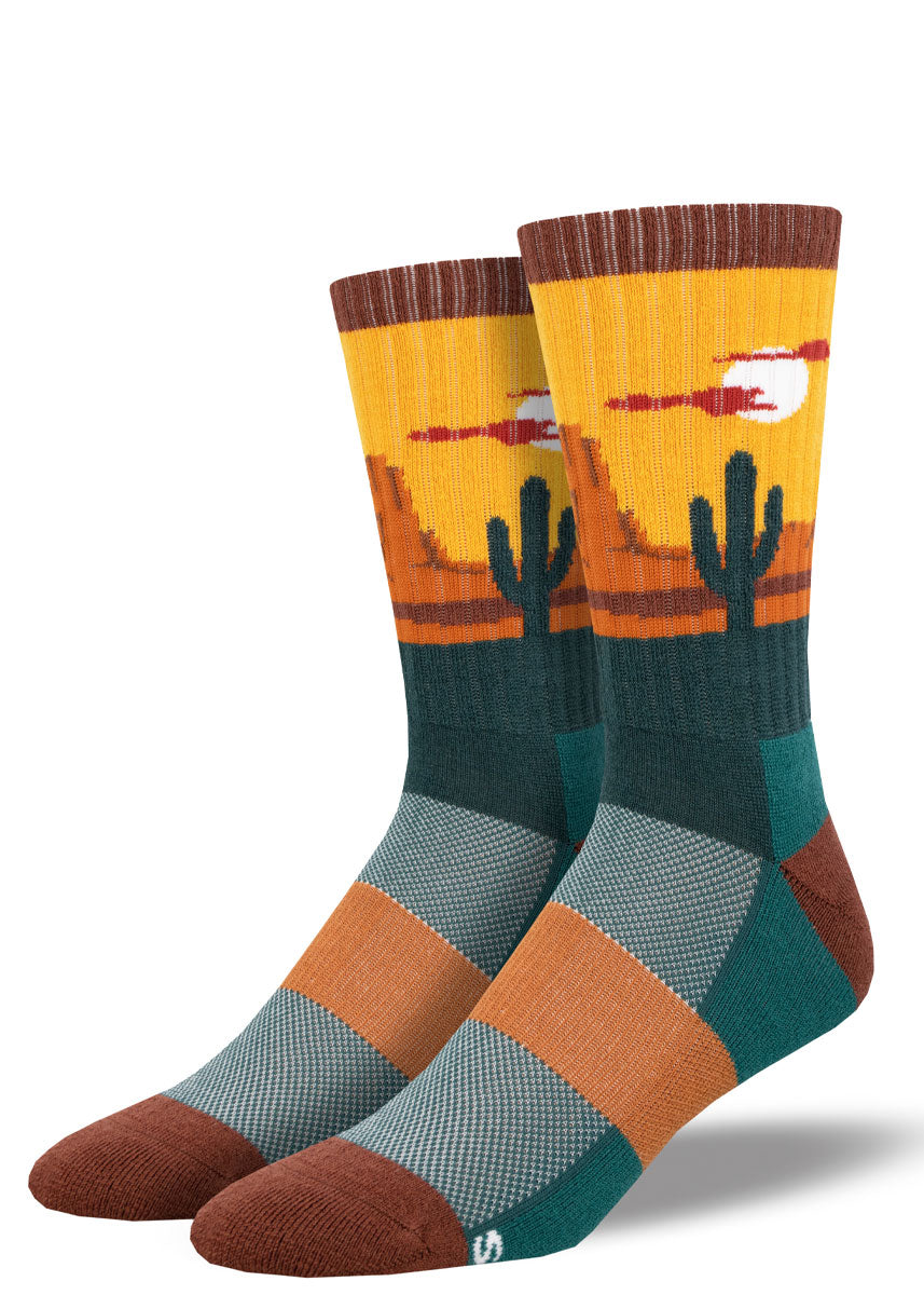 Yellow, orange, and dark green wool hiking socks for men feature a desert landscape scene with cacti and sandy dunes.