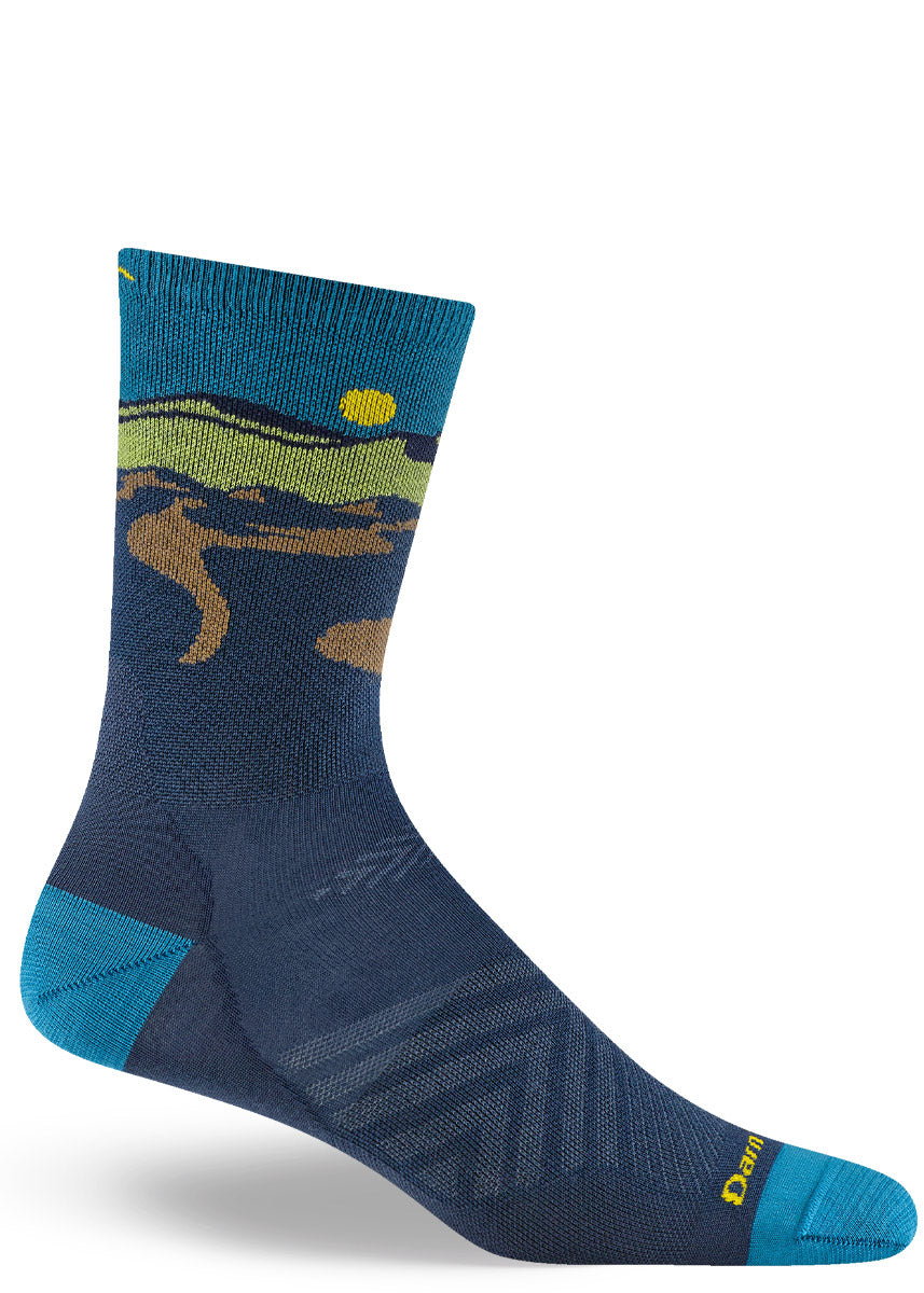 Dark blue lightweight hiking socks for men with a green and brown mountain landscape against a teal sky with a yellow sun. 