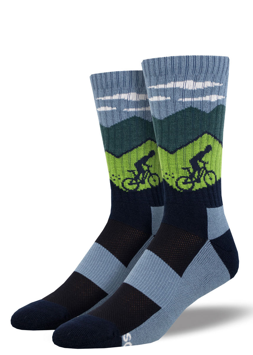 Blue, green, and black striped hiking socks for men that depict a mountain biker silhouette against a green mountain landscape and blue cloudy sky.