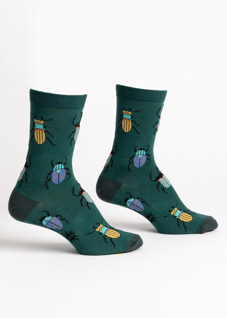 Dark green crew socks for women featuring a repeating pattern of yellow, teal, blue, and orange beetles with some blue and rainbow shimmer elements.