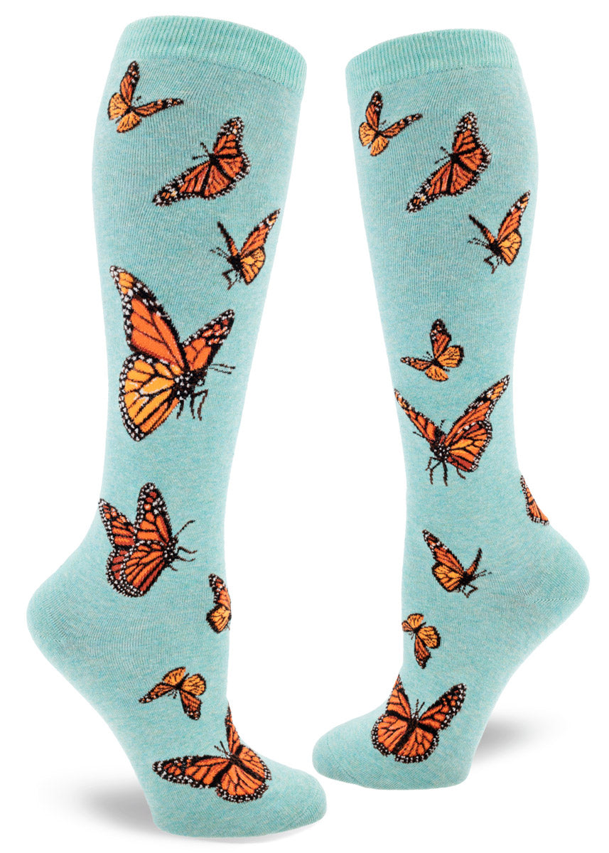 Light blue knee socks for women with an allover pattern of orange monarch butterflies in various poses in flight.