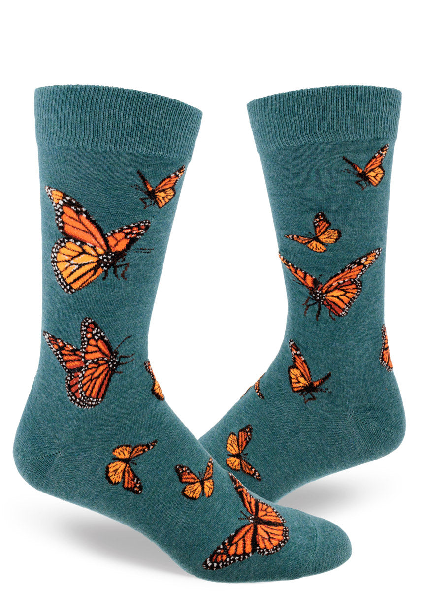 Dark teal crew socks for men with an allover pattern of orange monarch butterflies in various poses in flight.