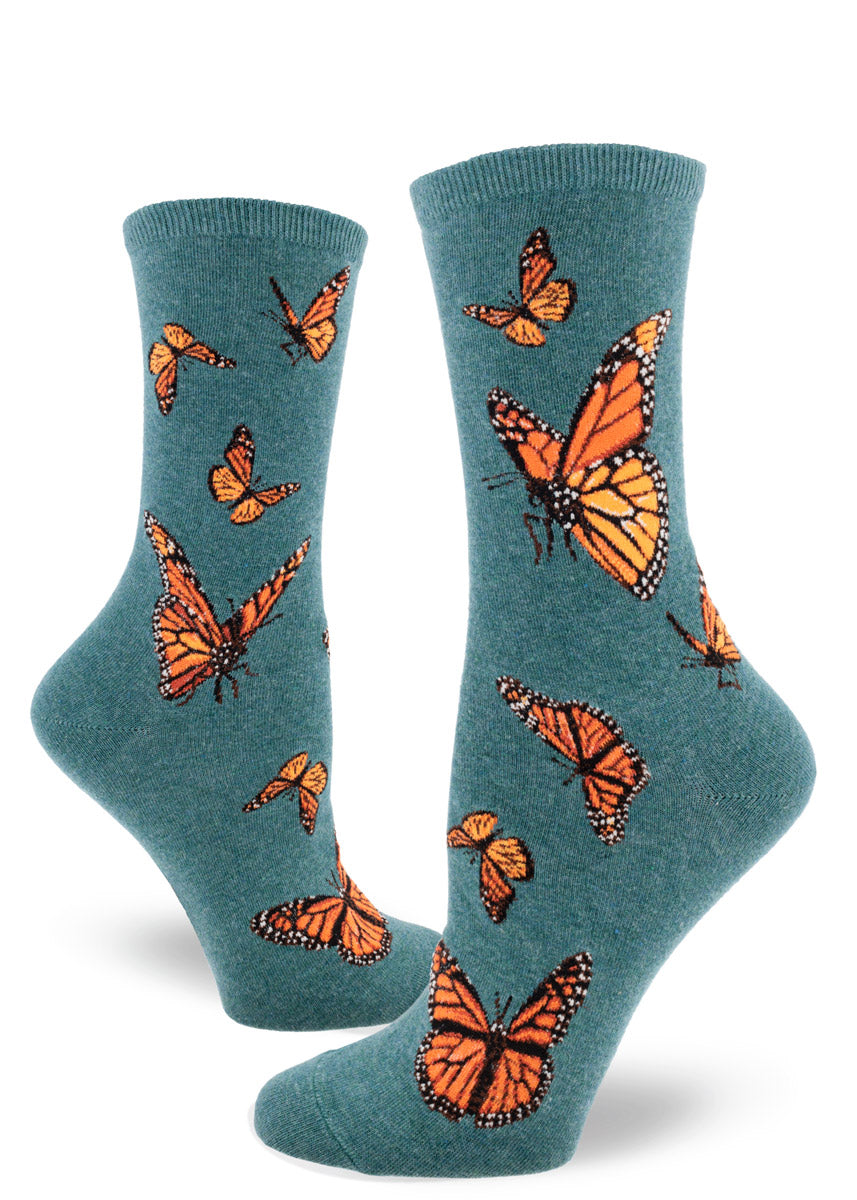 Dark teal crew socks for women with an allover pattern of orange monarch butterflies in various poses in flight.