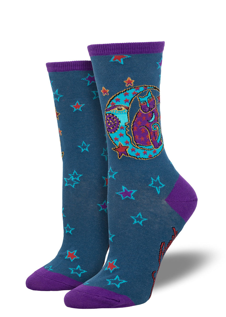 Blue crew socks for women designed by the artist Laurel Burch that feature a colorful cat sitting on a crescent moon along with stars in a color palette of purple, red, and blue. 
