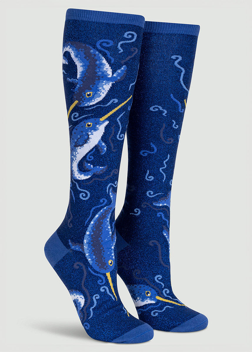 Deep blue shimmering knee socks are embellished with a swimming narwhal motif accented by swirling wave designs.
