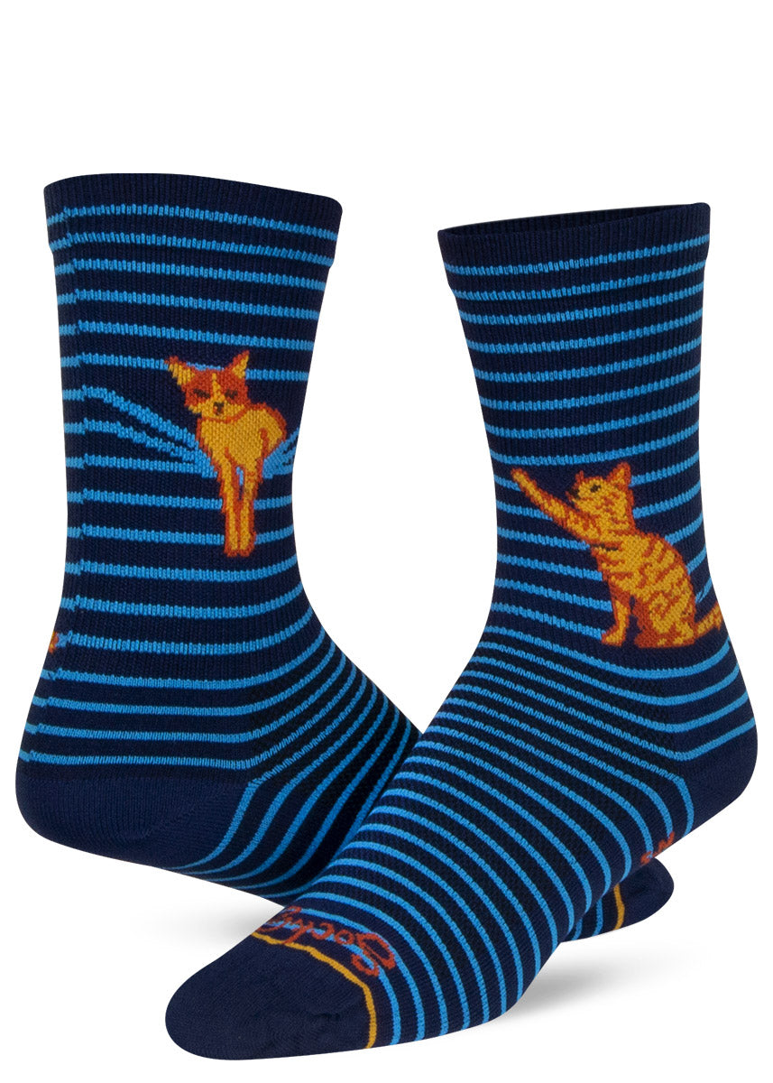 Black and blue striped crew socks show an orange cat laying in and playing with the stripe pattern as if the stripes were window blinds.