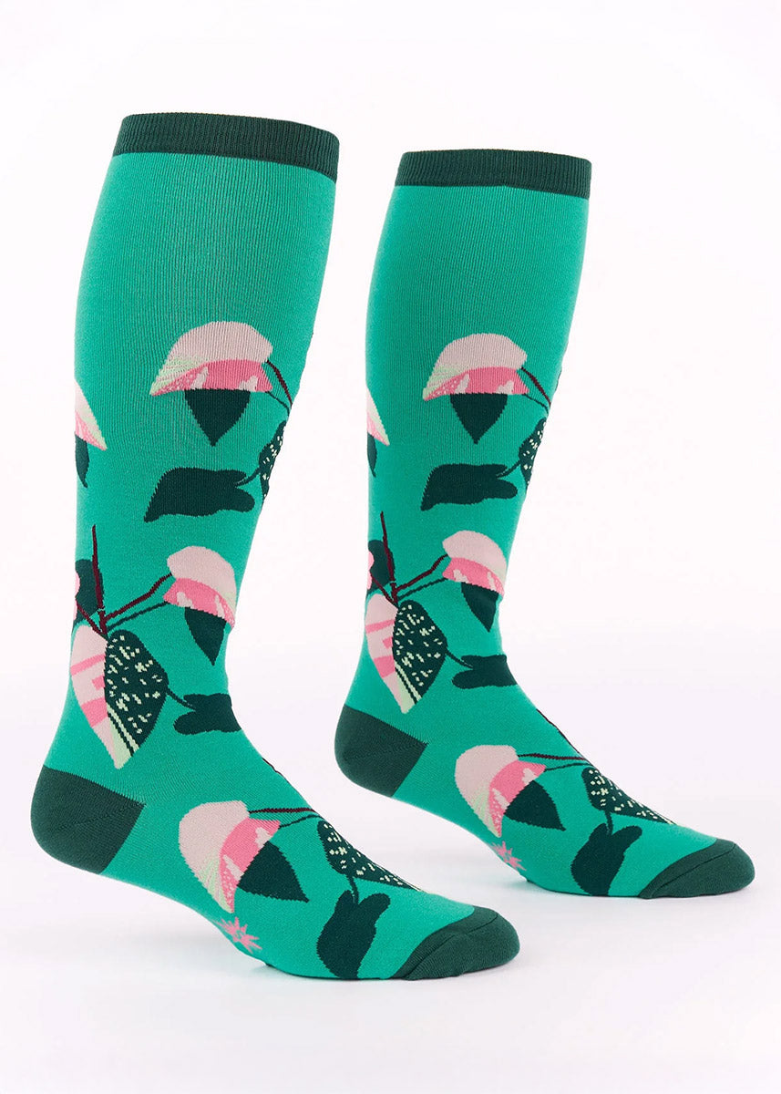 Teal knee socks with a pink and green  philodendron houseplant design on a white background.