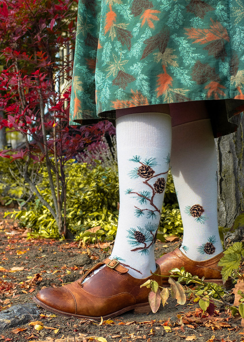 Knee high socks for women feature bending pine branches covered in pinecones and pine needles.