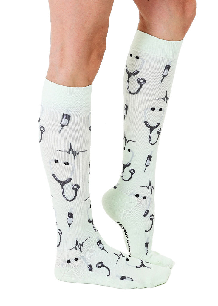A side view of pale mint green knee-high compression socks with an allover pattern in a medical theme including stethoscopes, syringes and more.