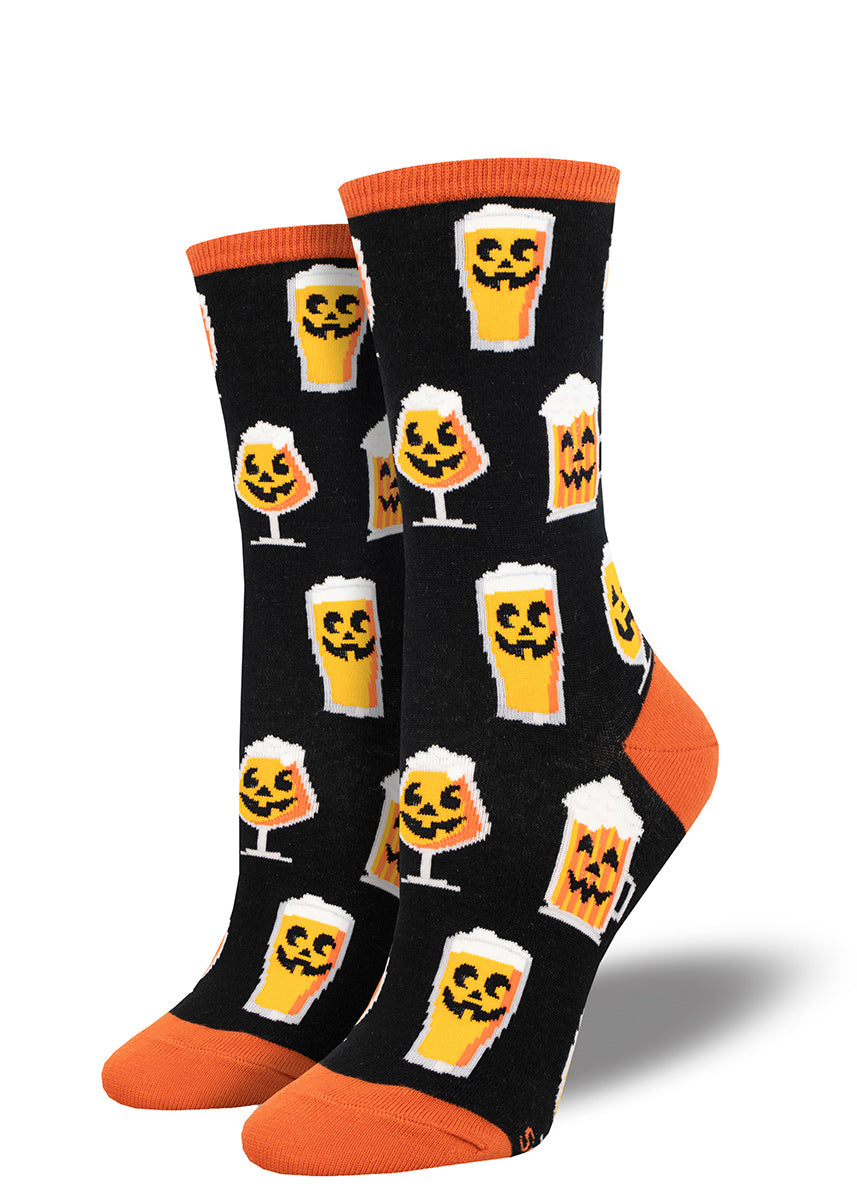 Black crew socks for women with orange accents and an allover pattern of glasses of pumpkin beer with smiling jack-o-lantern faces.